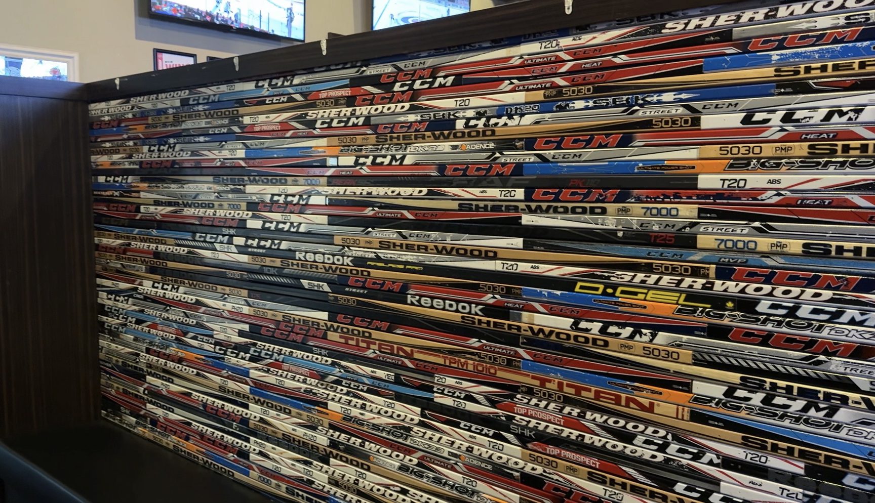 The back of a waiting bench built from dozens of hockey sticks laid horizontally, brand names and model numbers facing out