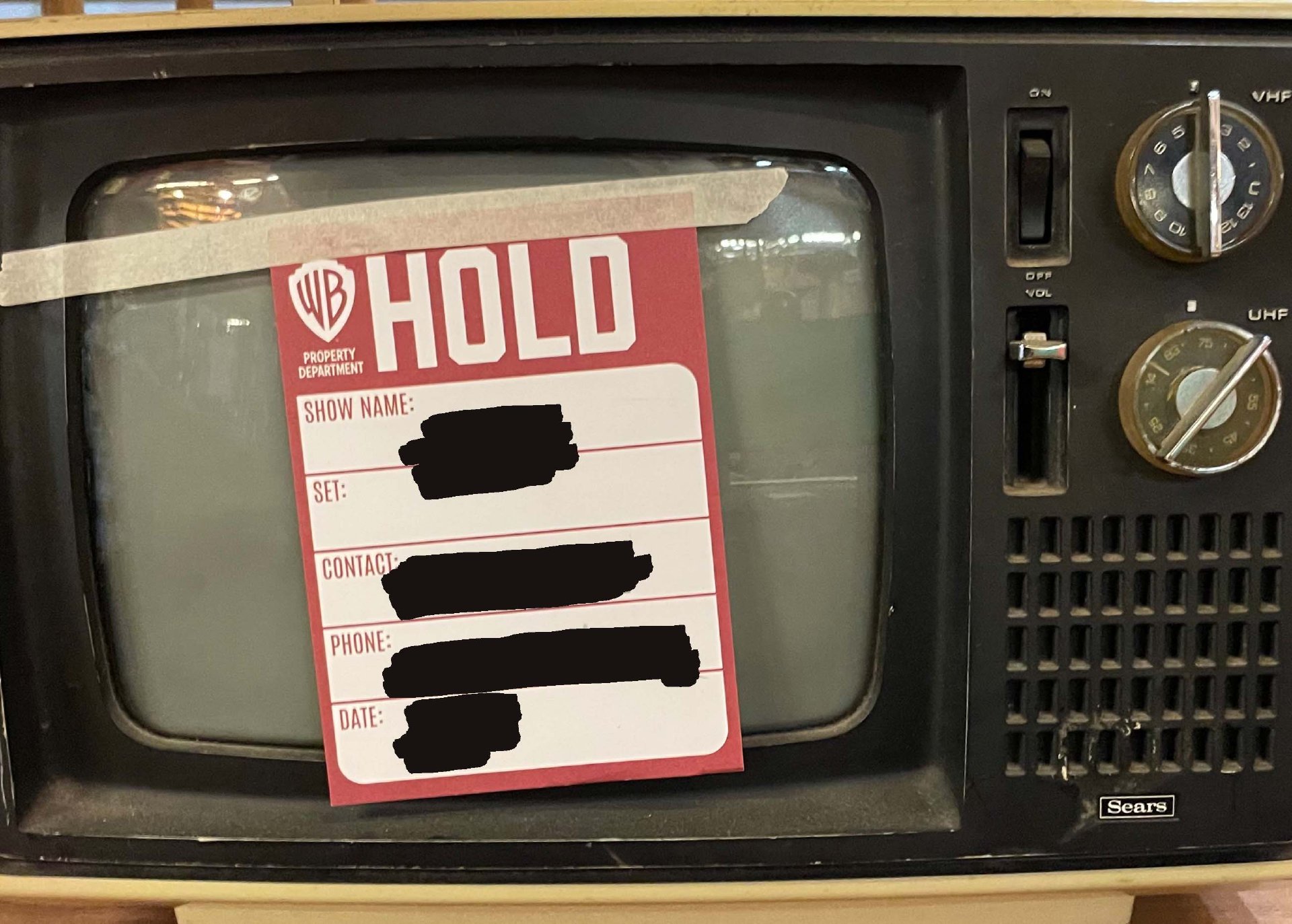 A small Sears black-and-white television with a Warner Bros. Property Department hold tag taped across the screen.